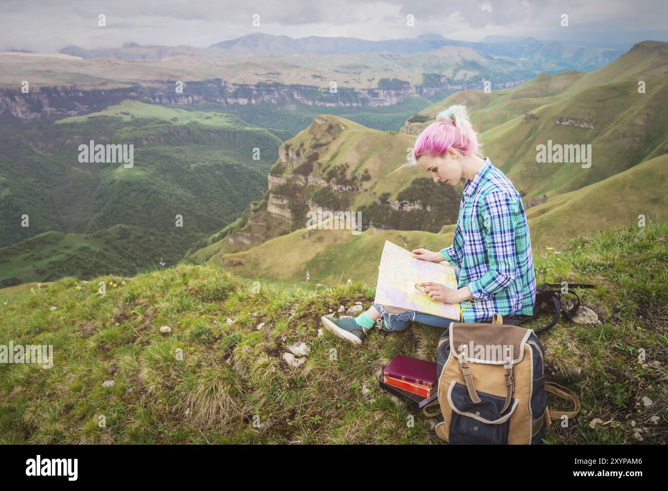 Mädchen mit mehrfarbigem Haar, das auf einer Naturlesekarte sitzt und einen Kompass in der Hand hält. Das Konzept der Navigation in der Suche und Tourismus i Stockfoto