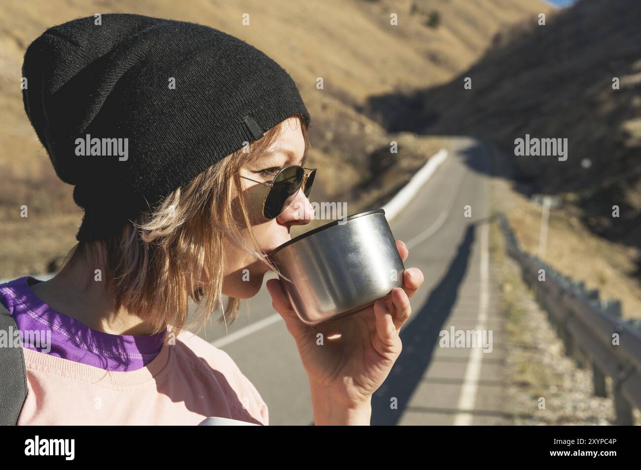 Ein Hipster-Mädchen mit Sonnenbrille und schwarzem Hut trinkt Tee oder Kaffee aus einer Tasse aus einer Thermoskanne in freier Wildbahn auf einer Reise Stockfoto