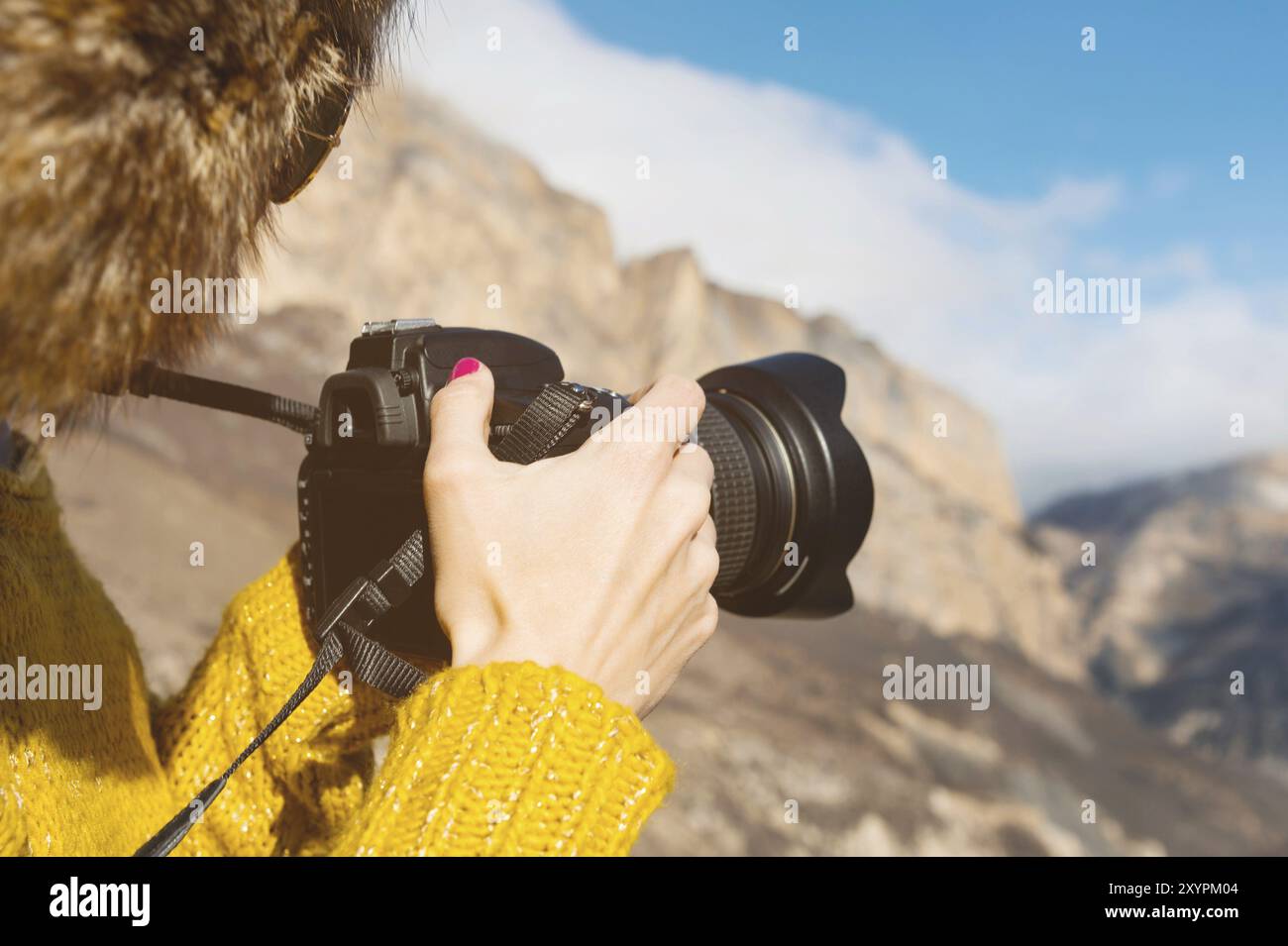 Eine Touristenfotografin mit Pelzmütze und gelbem Pullover in den Bergen macht Fotos mit ihrer Digitalkamera. Der Begriff der Fotografie auf der Reise Stockfoto