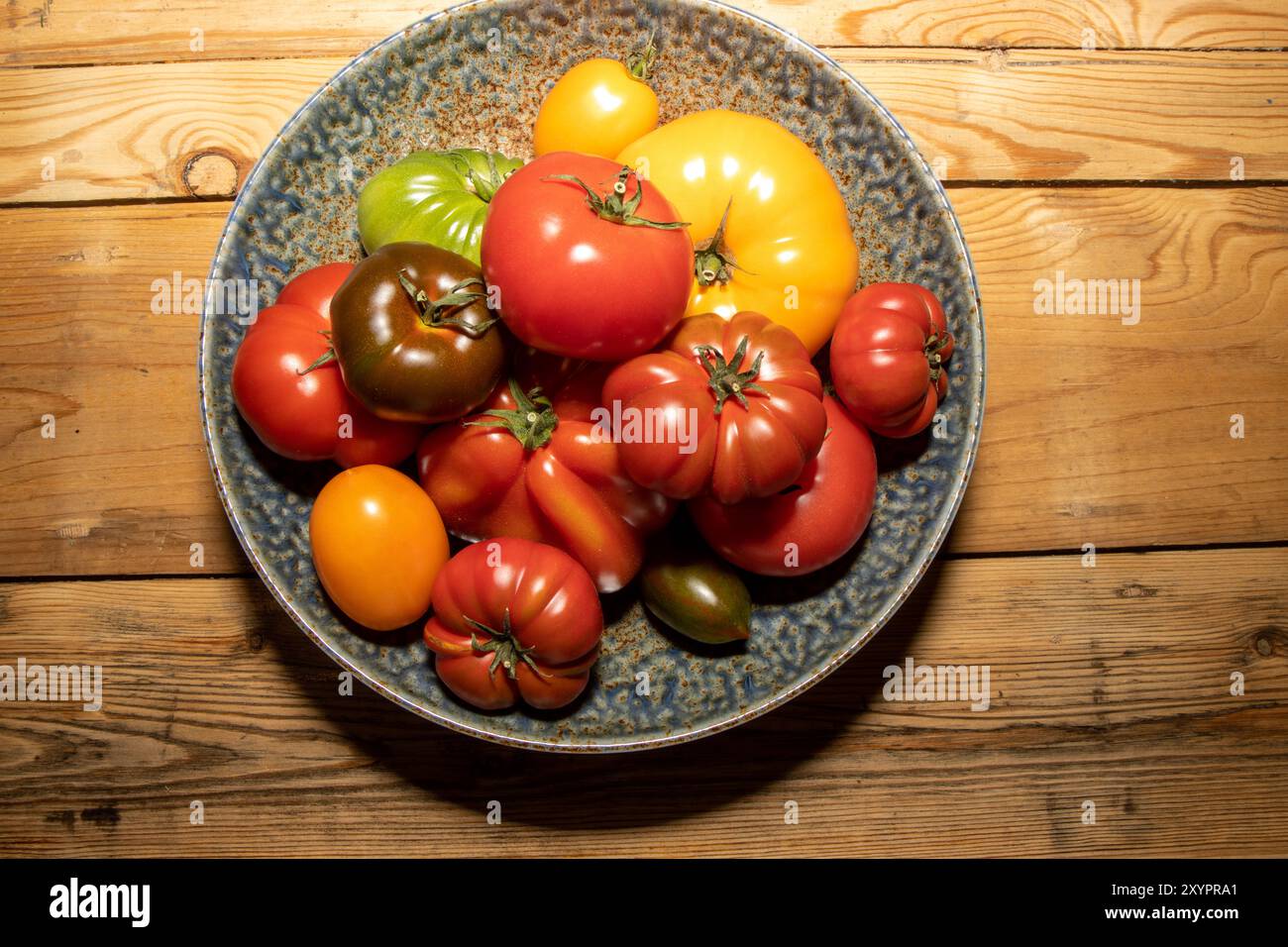 Eine Schüssel mit verschiedenen Größen und Farben Tomaten auf einem Küchentisch aus Holz Stockfoto