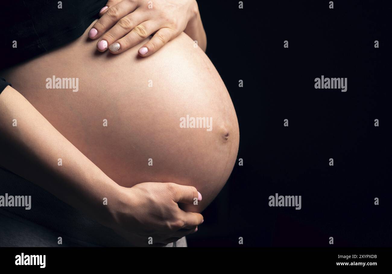 Bauch einer schwangeren Frau von der Seite. Dunkler Hintergrund, Kopierbereich Stockfoto