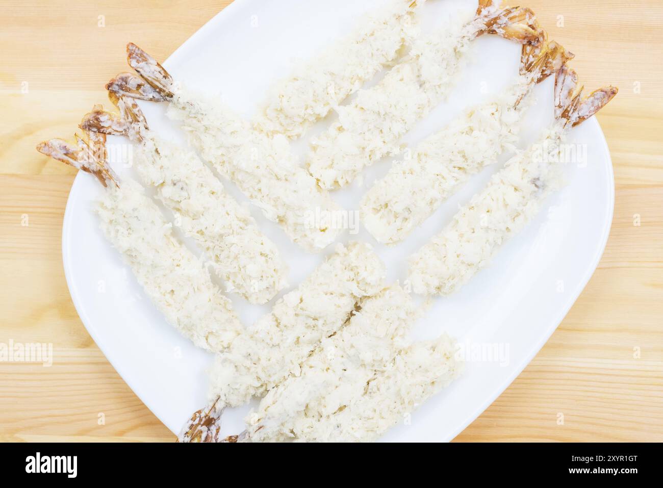 Nahaufnahme von rohen Tempura-Garnelen in panierter Form lag auf einem weißen Teller, der auf einem Holztisch steht. Halbfertige Meeresprodukte für die Hausmannskost Stockfoto