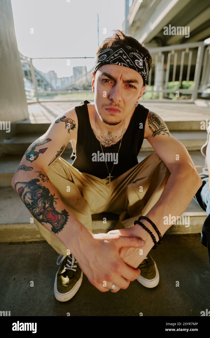 Junger brutaler, rauer Mann, der auf der Treppe sitzt und in die Kamera schaut Stockfoto