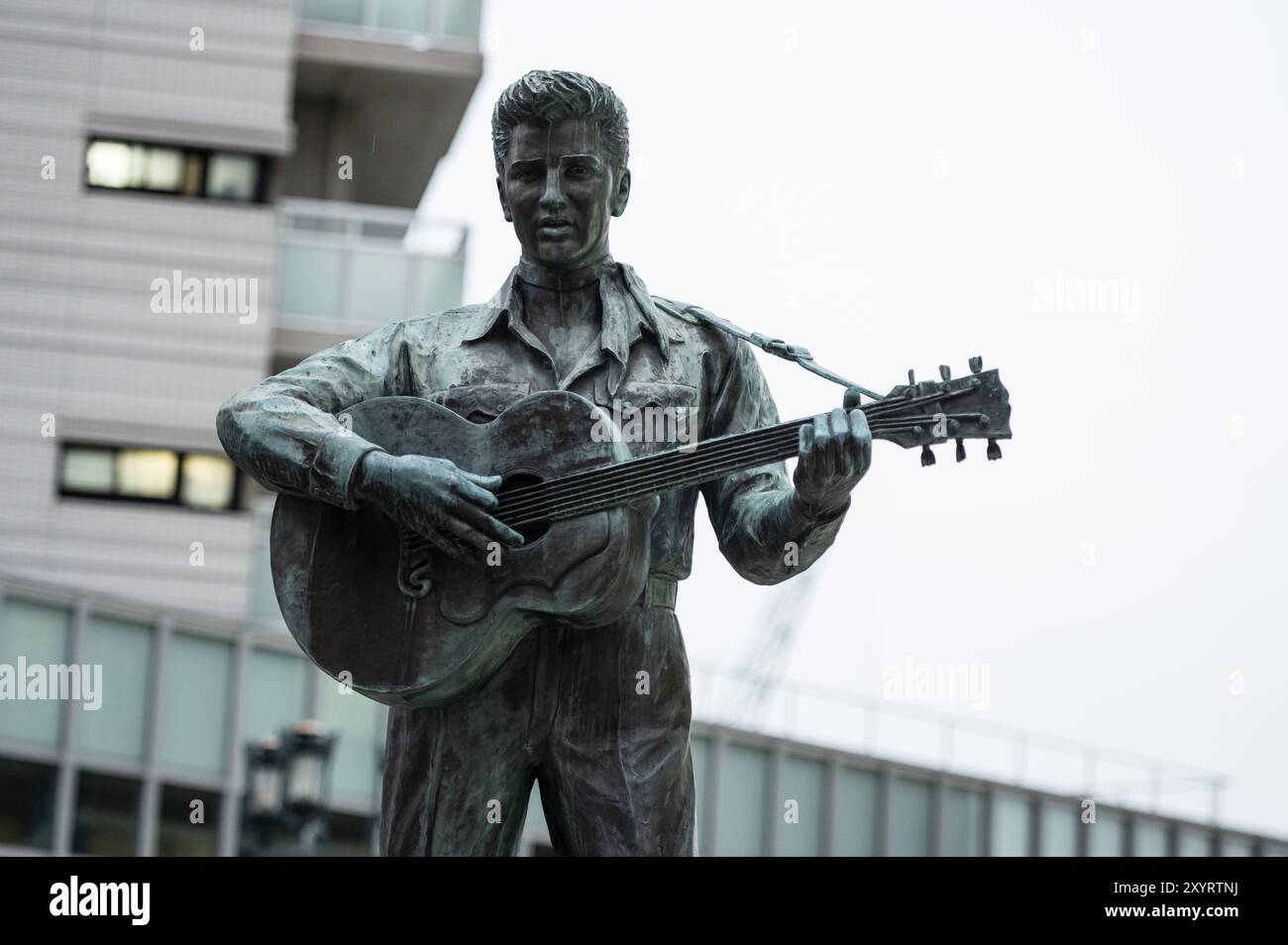 Eine Bronzestatue des Gitarrenspielers Elvis Presley, aufgenommen in einer urbanen Umgebung. Die Statue mit klassischer Kleidung steht als Stockfoto