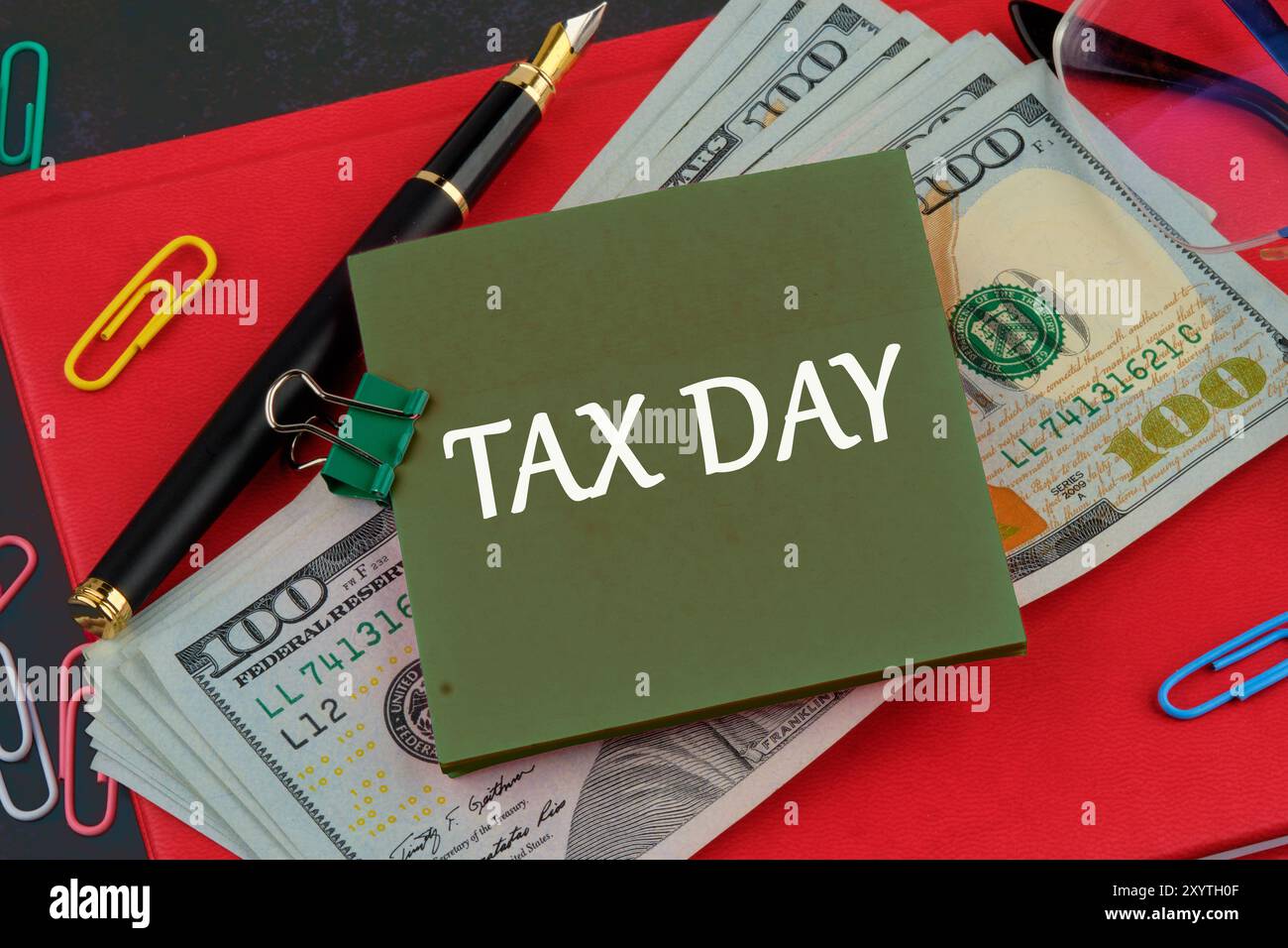 Tax Day Tax Financial Money Money Konzept. "STEUERTAG" auf einem grünen Aufkleber auf dem Hintergrund amerikanischer Dollars und einem roten Geschäftsbuch Stockfoto