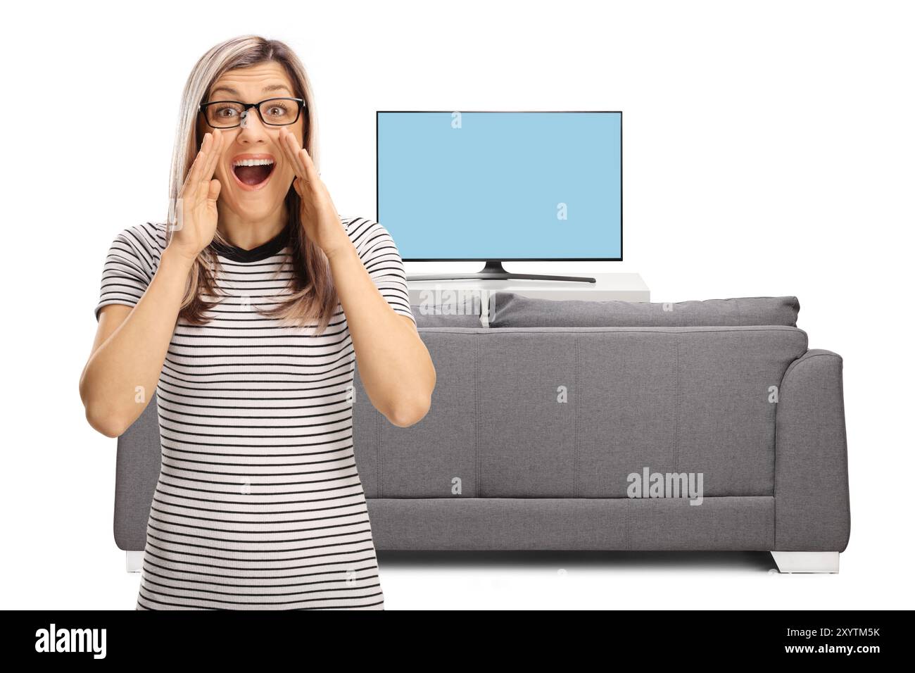 Blonde Frau mit Brille, die vor dem fernseher und dem Sofa auf weißem Hintergrund brüllt Stockfoto