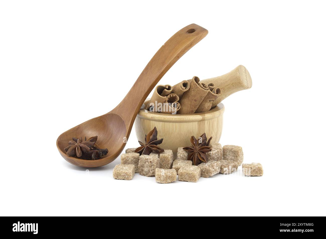 Sternanis in einem Holzlöffel, Holzmörtel gefüllt mit Zimtstangen und braunen Zuckerwürfeln isoliert auf weißem Hintergrund Stockfoto