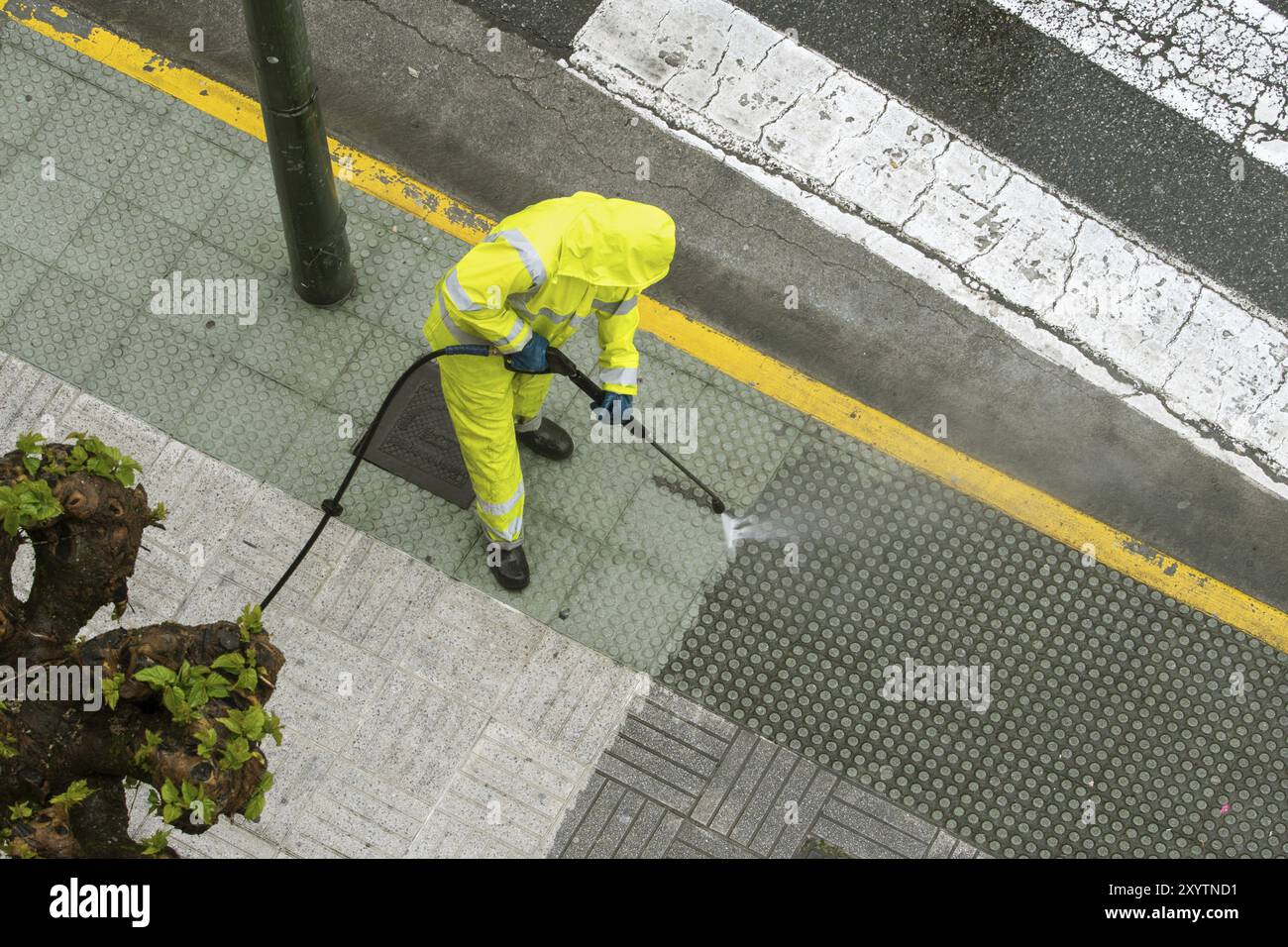 Blick von oben auf ein Arbeiter die Straße Gehweg mit Hochdruck Wasserstrahl reinigen. Öffentliche Wartungskonzept Stockfoto