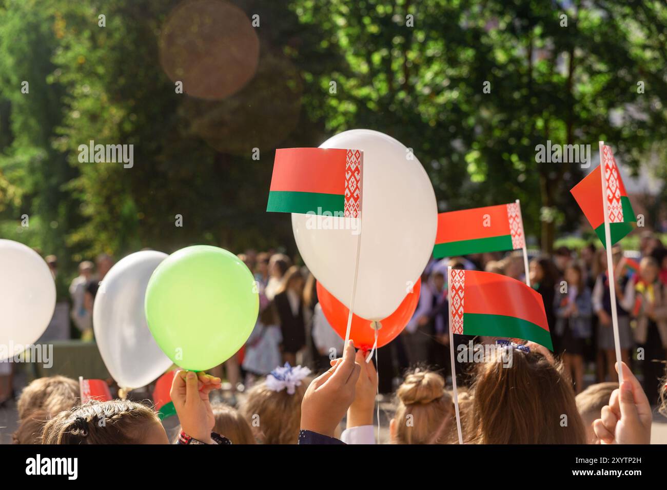 Ein feierliches Treffen in der Nähe der Schule, das dem Tag des Wissens in der Republik Belarus gewidmet ist. Kinder halten nationale Symbole, Fahnen und rote Bälle Stockfoto