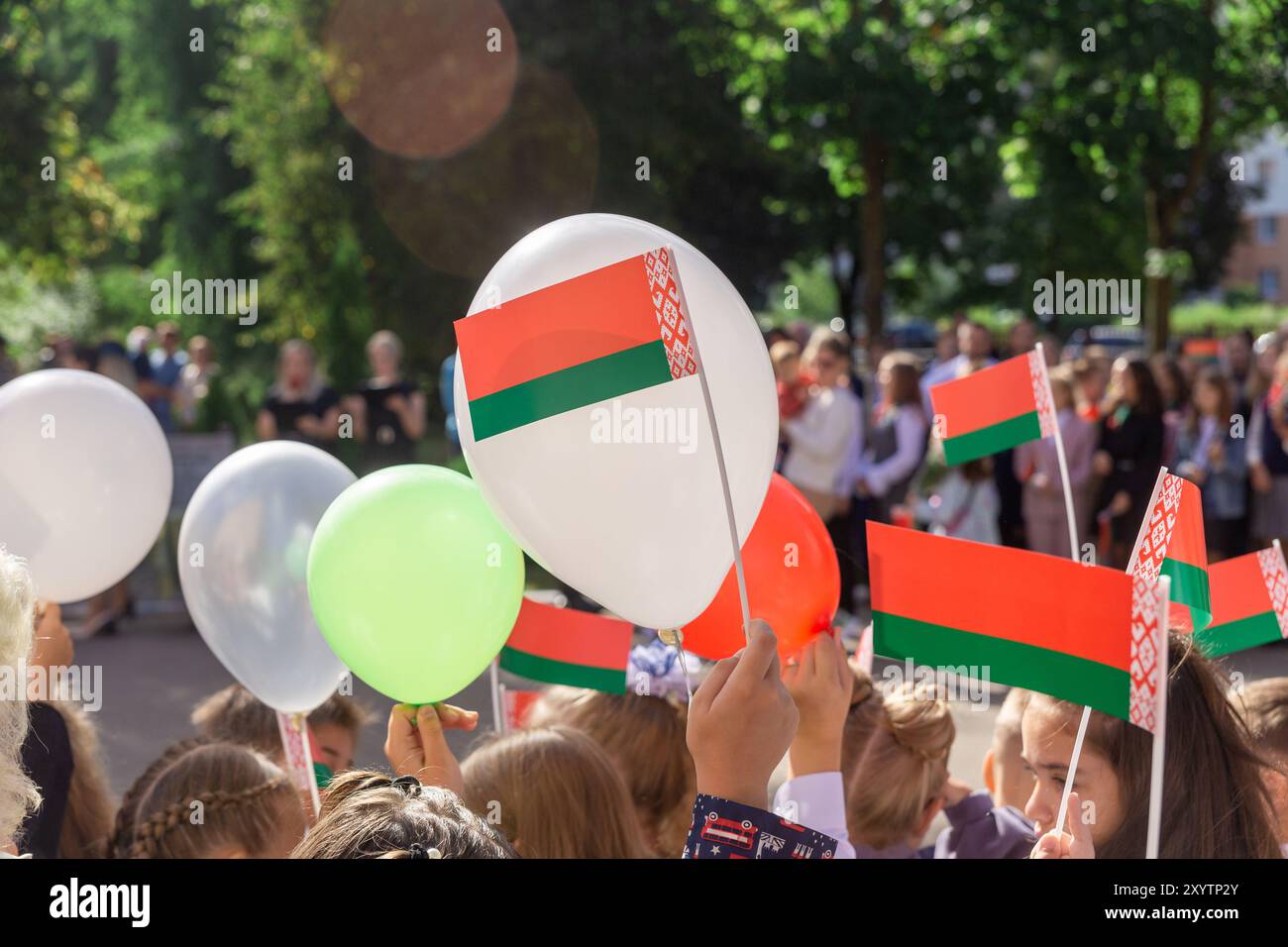 Ein feierliches Treffen in der Nähe der Schule, das dem Tag des Wissens in der Republik Belarus gewidmet ist. Kinder halten nationale Symbole, Fahnen und rote Bälle Stockfoto