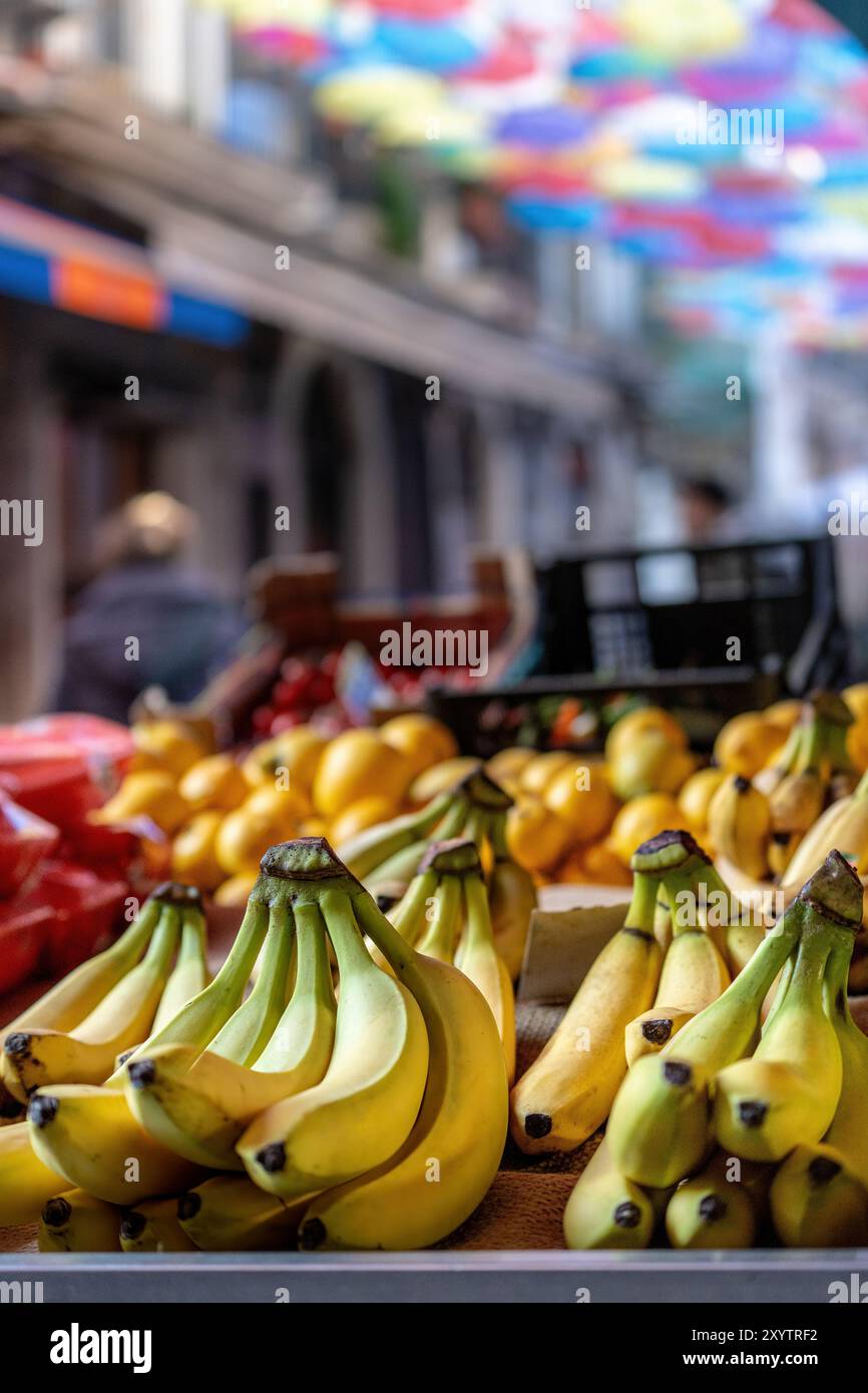 Frische Bananen werden auf einem lebhaften Obstmarkt in Catania präsentiert, mit farbenfrohen Regenschirmen, die ein lebendiges Baldachin bilden. Fängt das Wesen von Si ein Stockfoto