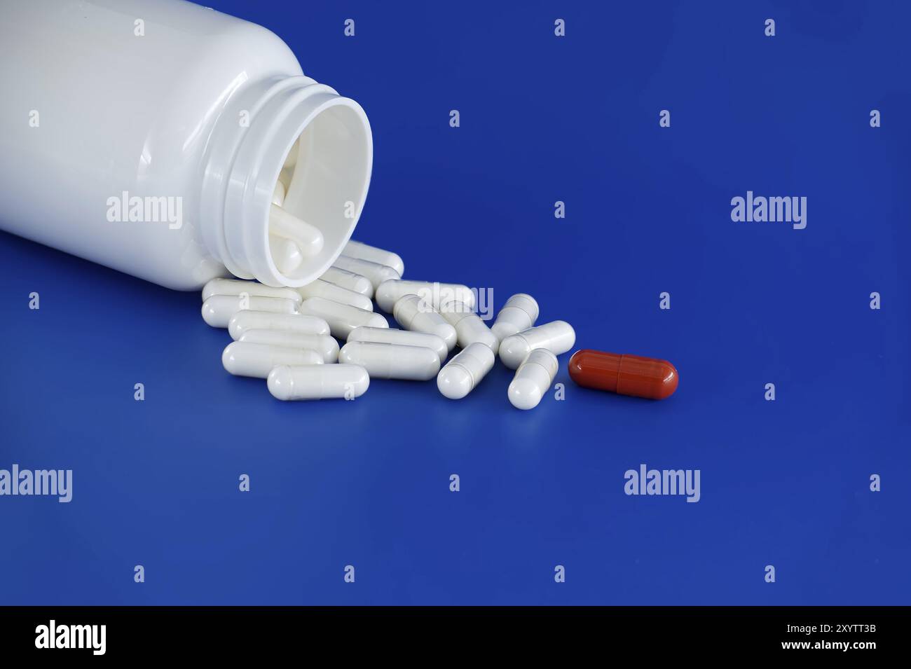Umgedrehte weiße Arzneimittelflasche mit ihrem Inhalt weiße Tabletten oder Kapseln, auf blauem Hintergrund verschüttet. Unter diesen weißen Pillen, eine einsame Re Stockfoto
