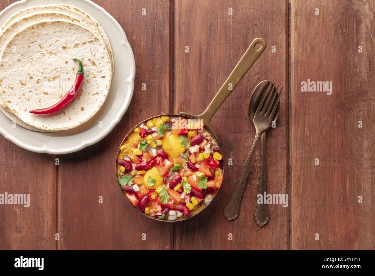 Huevos Rancheros, mexikanische Spiegeleier, von oben geschossen mit Pico de gallo Salat, Tortillas und einer roten heißen Chili-Pfeffer auf einem dunklen rustikalen Holzbackgr Stockfoto