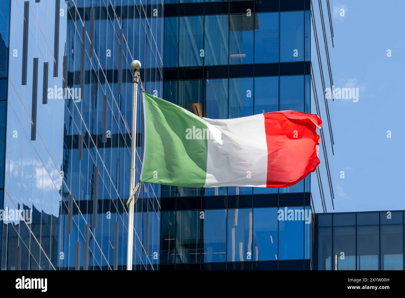 Eine italienische Nationalflagge, die im Wind winkt, mit einem Glasgebäude im Hintergrund. Stockfoto