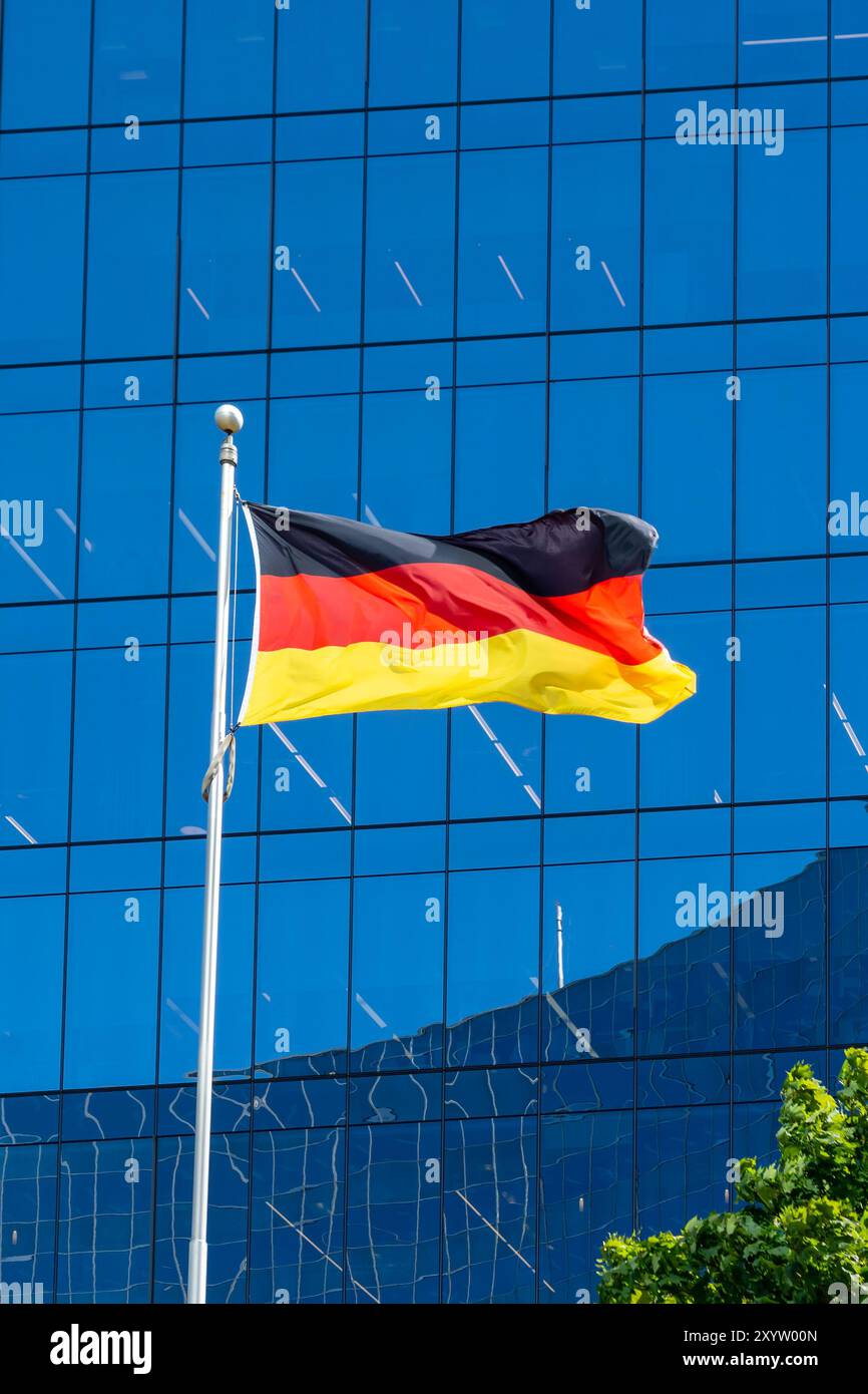 Eine Nationalflagge Deutschlands, die im Wind winkt, mit einem Glasgebäude im Hintergrund. Stockfoto