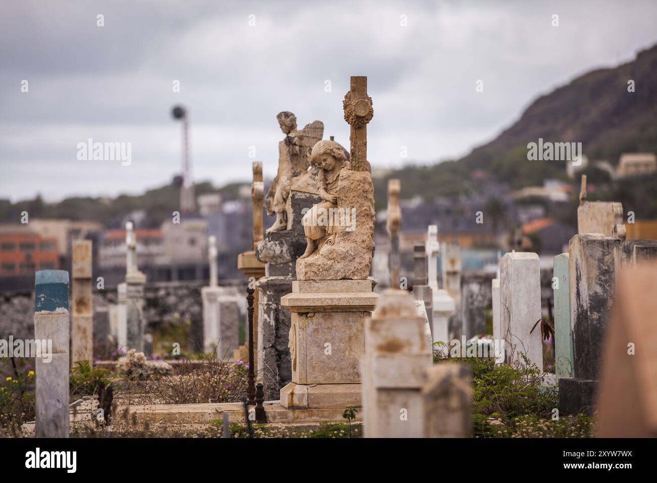 Grabstein auf einem großen Friedhof, das ein kleines engelhaftes Mädchen zeigt, das unter einem Kreuz sitzt und den Stein graviert Stockfoto