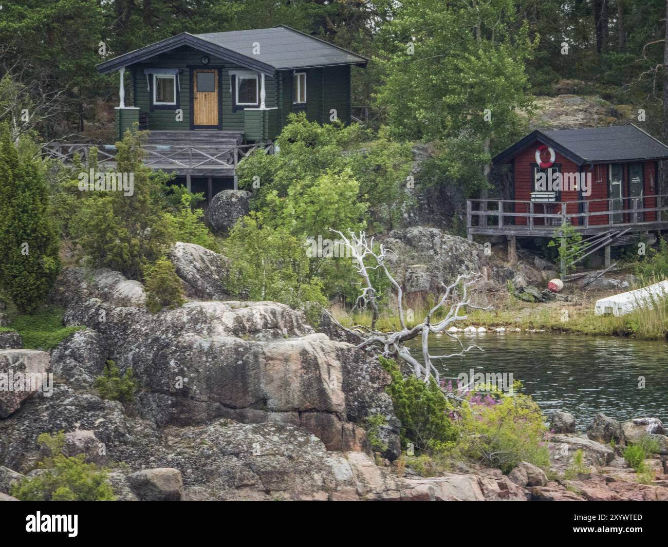 Zwei rustikale Holzhäuser stehen auf Felsen am Seeufer, umgeben von Wald und Wasser, stockholm, ostsee, schweden, skandinavien Stockfoto