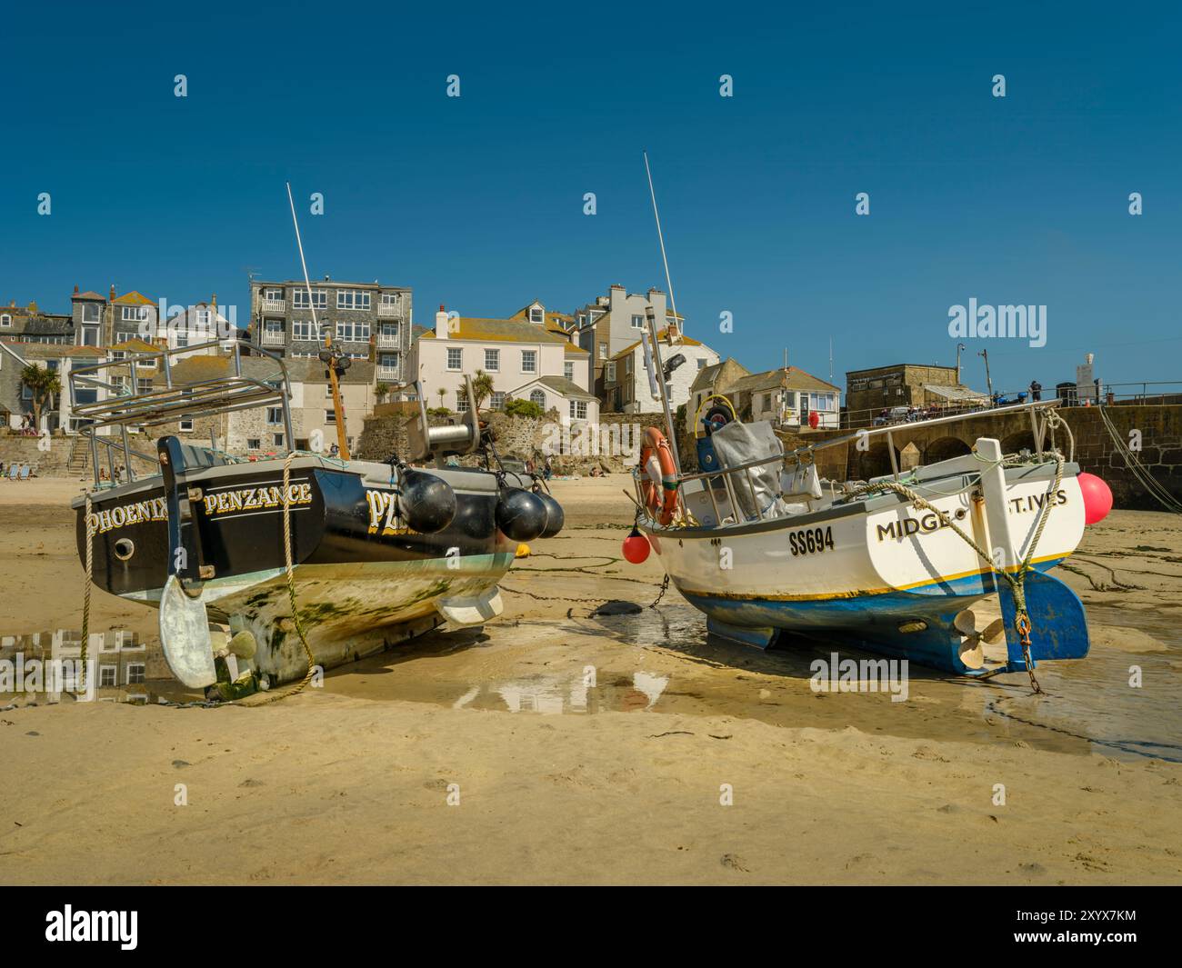 St Ives, Cornwall - an einem warmen Apriltag liegen bei Ebbe kleine Fischerboote auf dem goldenen Sand des Hafenstrandes von St Ives in Cornwall, England Stockfoto