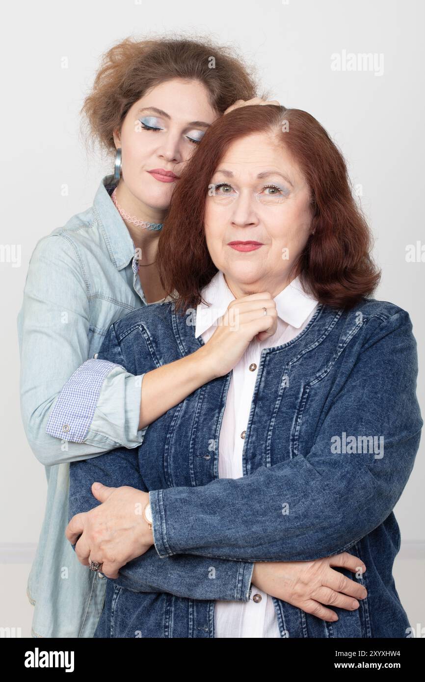 Eine ältere Mutter und eine Erwachsene Tochter schauen in die Kamera. Die Schwiegertochter umarmt sanft ihre Schwiegermutter. Stockfoto