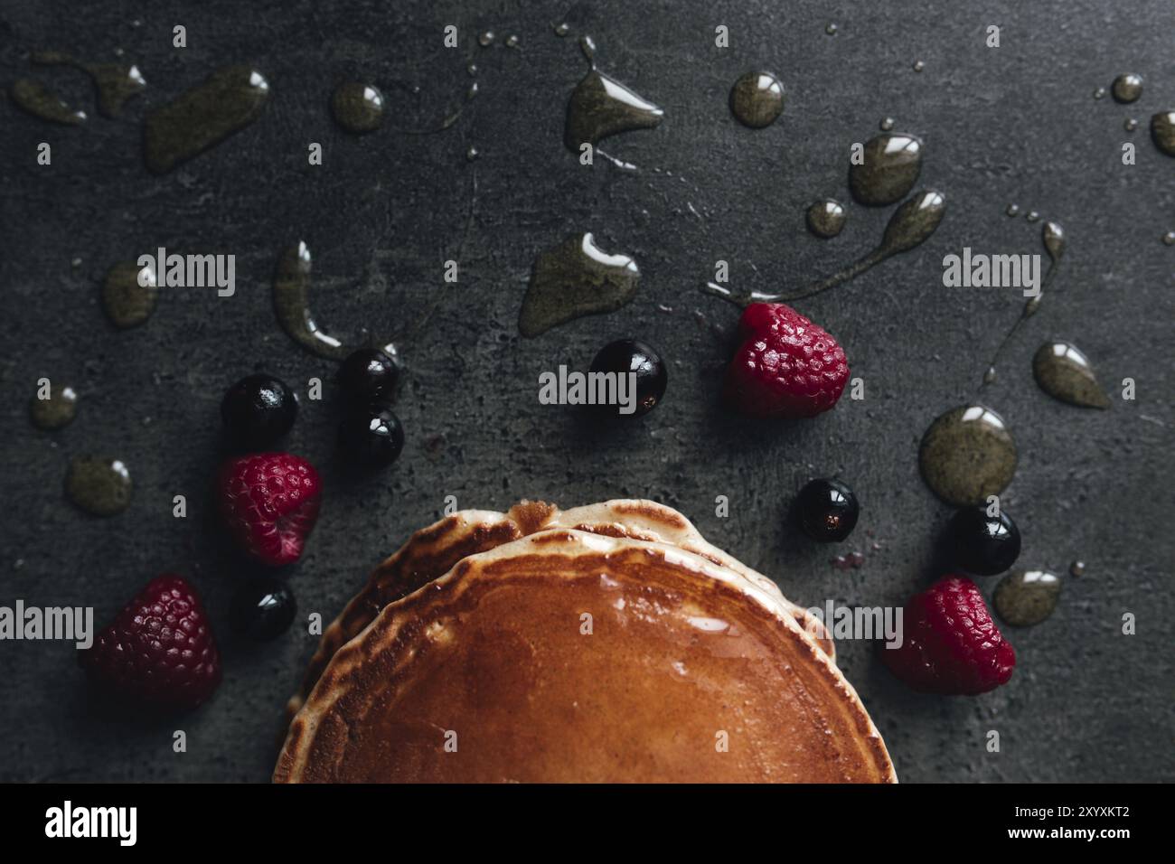 Saftige Pfannkuchen mit Beeren, Honig, Löffel auf einem schwarz-grauen Betontisch. Stockfoto
