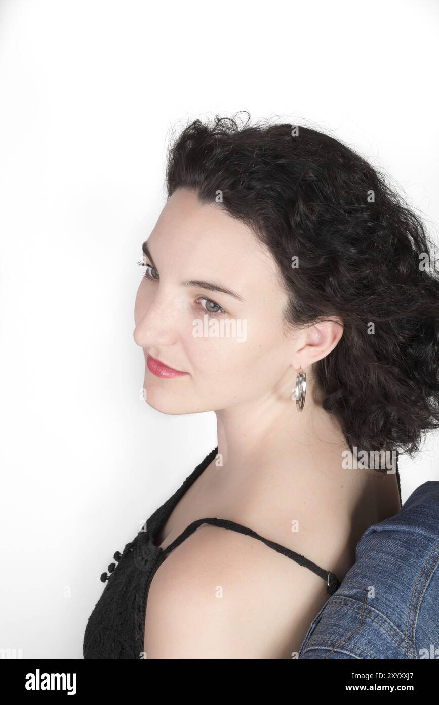 Junge Modell in ihrer Mitte der 20er Jahre sitzt auf einem Stuhl mit einer blauen Jeans Jacke hängt über der Stuhllehne Stockfoto