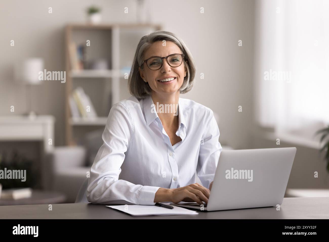 Glückliche Frau mittleren Alters sitzt im Home Office mit Laptop Stockfoto