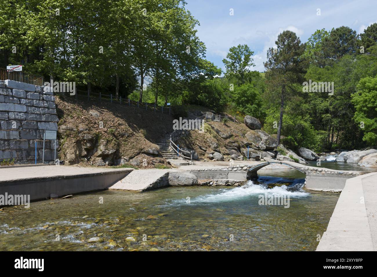 Ein ruhiger Fluss fliesst durch ein Gebiet mit einer kleinen Bruecke und einer Steintreppe, umgeben von Felsen und ueppigem Gruen, Piscinas naturales, Stockfoto