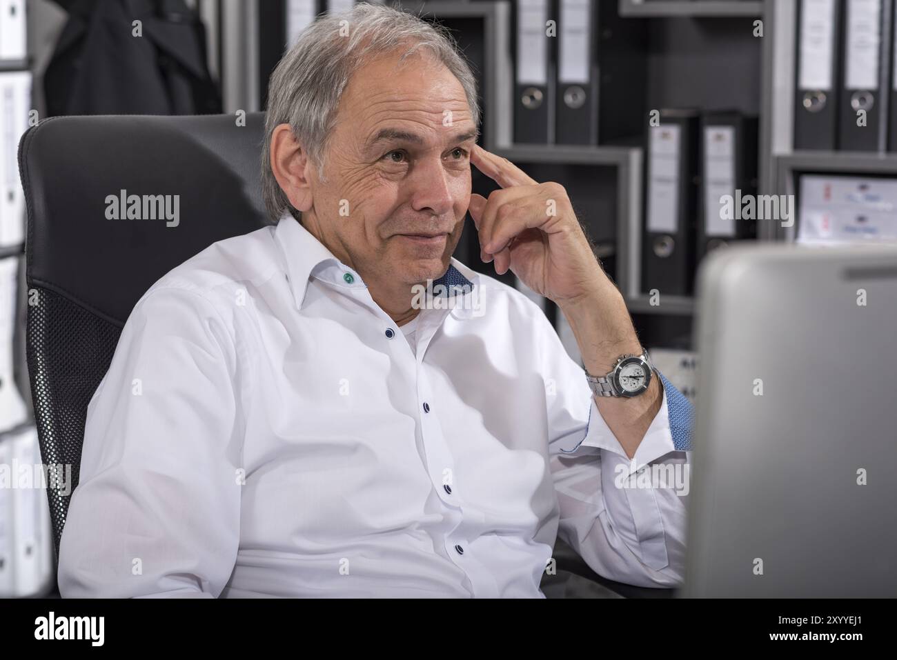 Lächelnder älterer Mann in einem weißen Hemd, der an einem Schreibtisch sitzt Stockfoto