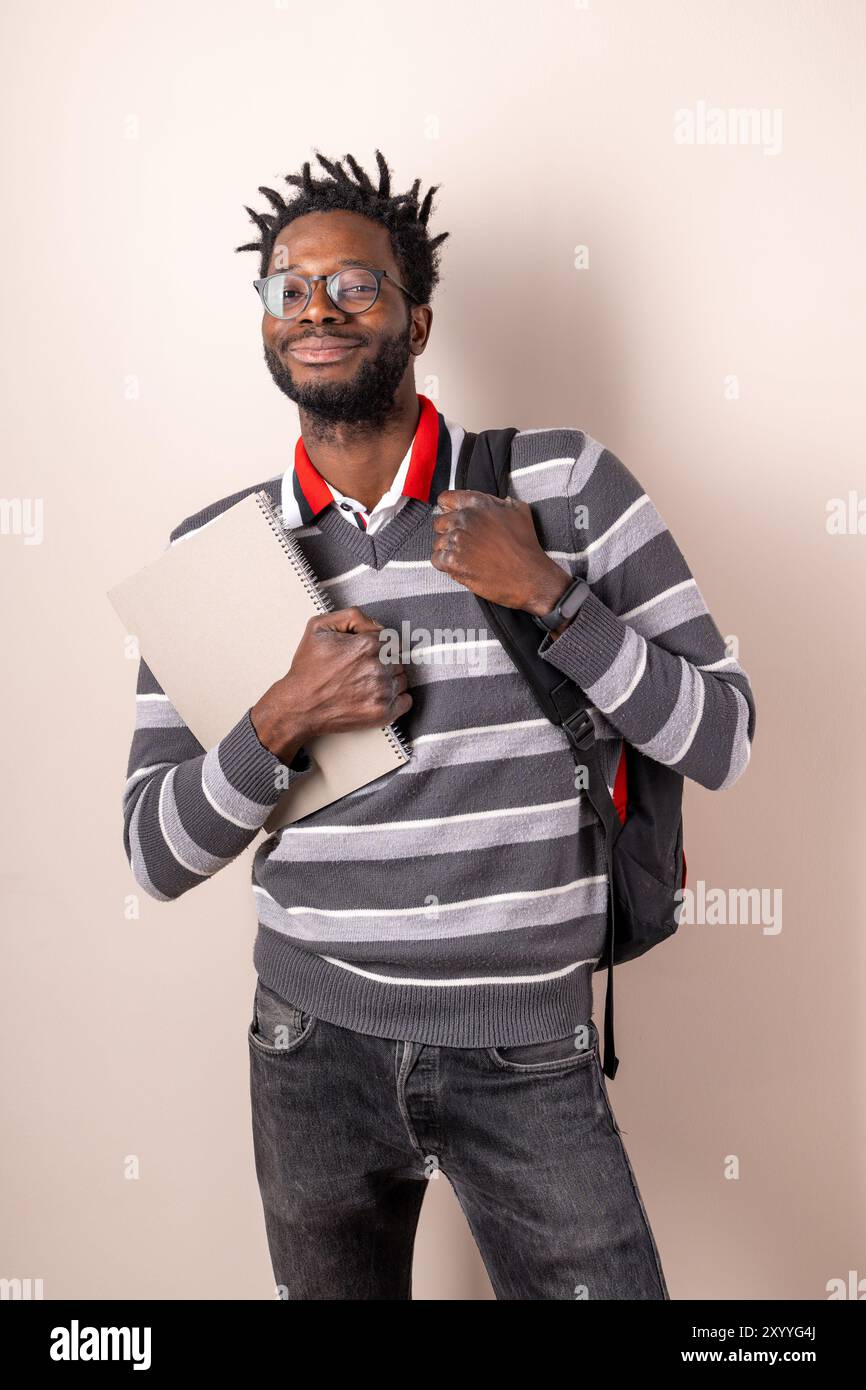 Lächelnder junger Afroamerikaner mit Brille und Dreadlocks, der Notebook hält und Rucksack trägt. Porträt eines selbstbewussten Studenten in Casua Stockfoto