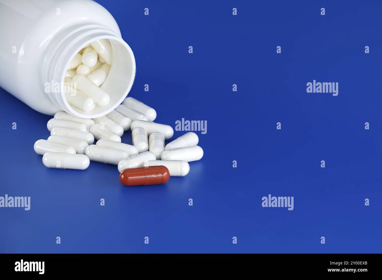 Umgedrehte weiße Arzneimittelflasche mit ihrem Inhalt weiße Tabletten oder Kapseln, auf blauem Hintergrund verschüttet. Unter diesen weißen Pillen, eine einsame Re Stockfoto