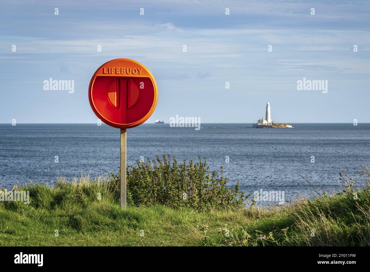 Ein leerer Rettungsschirm an der Nordseeküste in Seaton Sluice, Northumberland, England, Großbritannien, mit St. Mary's Lighthouse im Hintergrund Stockfoto