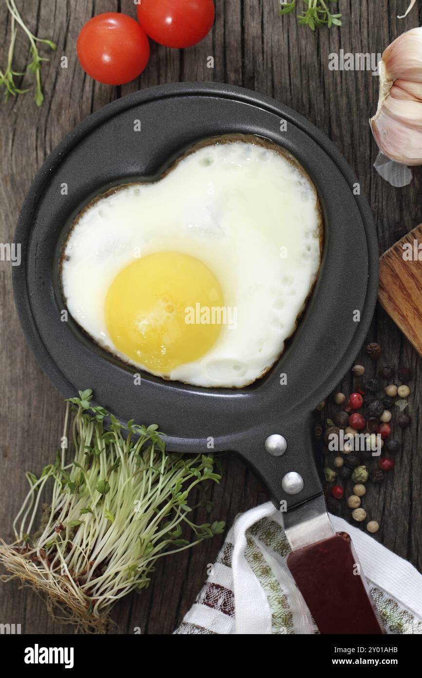 Spiegelei in Herzform Form mit Kresse, Tomaten, Knoblauch und Pfeffer Stockfoto