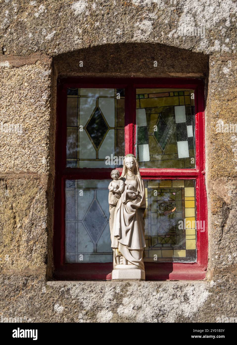 Lehon, Frankreich - 19. Juli 2024: Fenster des bretonischen Hauses mit geometrischen Mustern und Statue der heiligen Maria, die ein Kind Jesus hält. Stockfoto