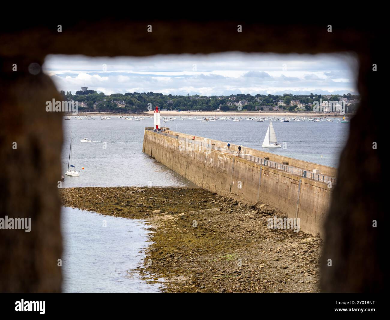 Saint Malo, Frankreich - 20. Juli 2024: Küstenszene in Saint Malo mit Leuchtturm, Ufermauer, felsiger Küste, Segelboot und beschaulichem Himmel. Durchschauen. Stockfoto