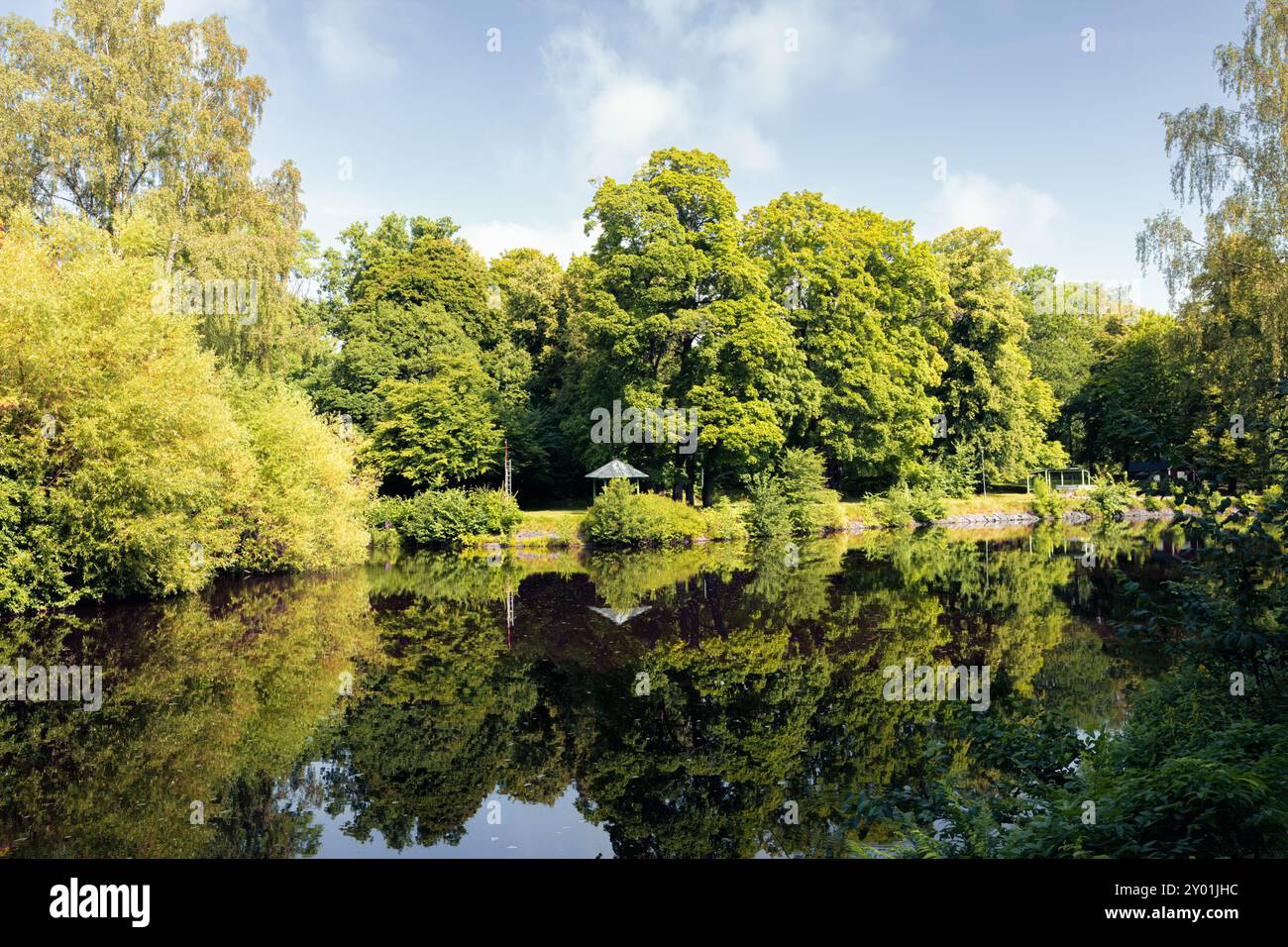 Üppiges Grün im Stadtpark mit hohen Bäumen und Reflexionen im Fluss Svartån. Entspannung und urbanes Entspannungskonzept. Orebro, Schweden. Leerzeichen für Text Stockfoto