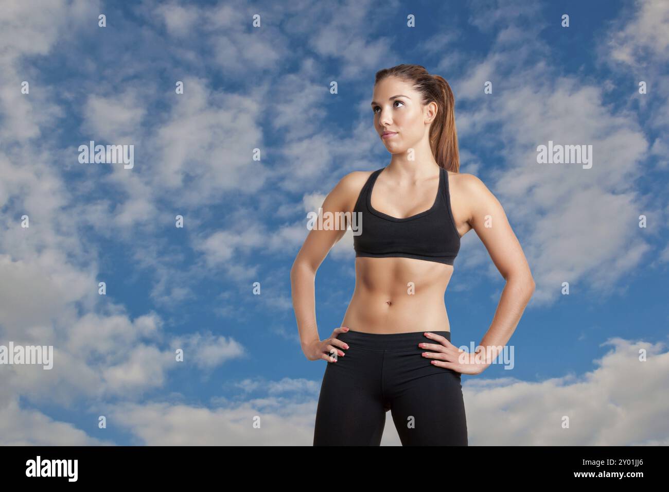 Sportliche Frau, die Arme ruhen auf ihre Taille mit einem wolkigen Himmel hinter ihr stehend Stockfoto