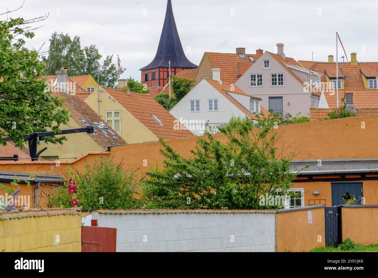 Gebäude mit orangefarbenen Dächern und markantem Turm in einem Dorf, bewölkter Himmel, Svaneke, bornholm, ostsee, dänemark, skandinavien Stockfoto