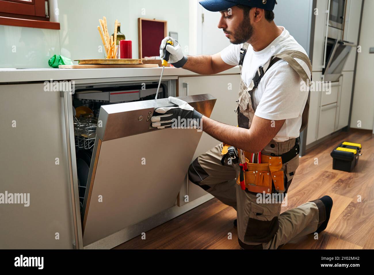 Professioneller Servicearbeiter, der Geschirrspüler in der Küche repariert, während Spezialwerkzeuge verwendet werden Stockfoto