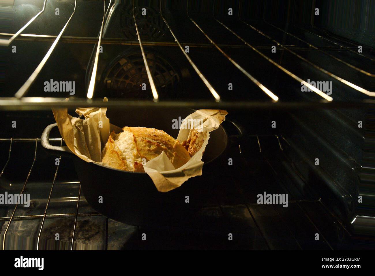 Schräg von oben auf ein schwarzes holländisches Brot mit goldener Kruste und Pergamentpapier in einem offenen Ofen bei eingeschaltetem Licht. Sitzt auf dem Backofen im Inneren Stockfoto