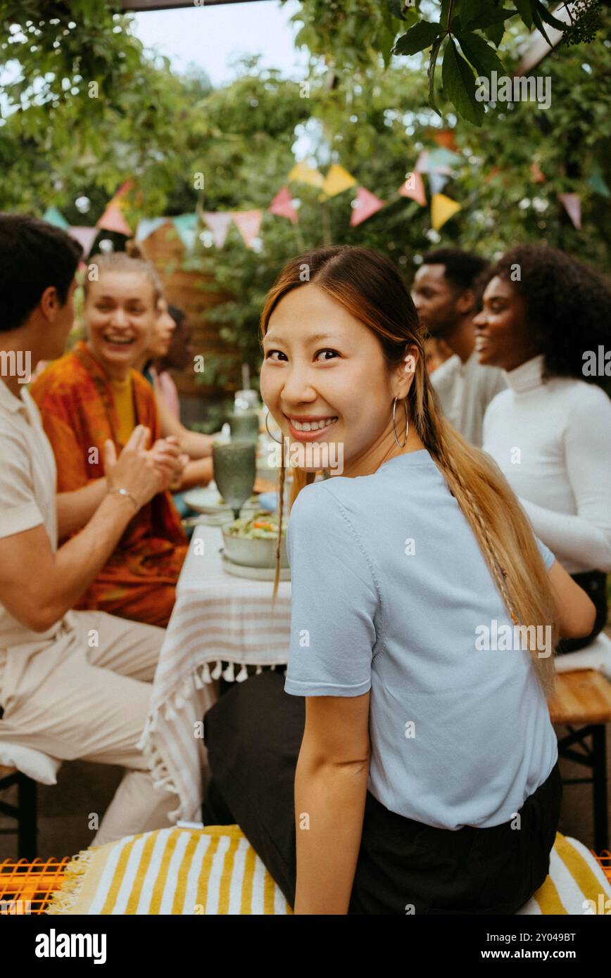 Lächelnde Frau, die während der Party mit Freunden am Esstisch sitzt Stockfoto