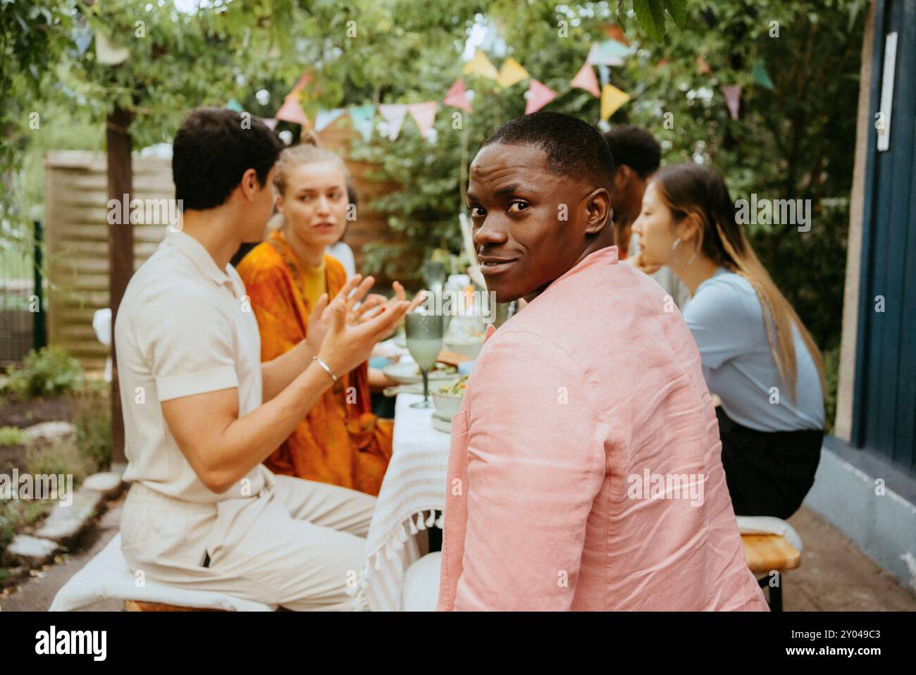 Porträt eines lächelnden Mannes, der über die Schulter schaut, während er mit Freunden sitzt und bei der Dinnerparty feiert Stockfoto