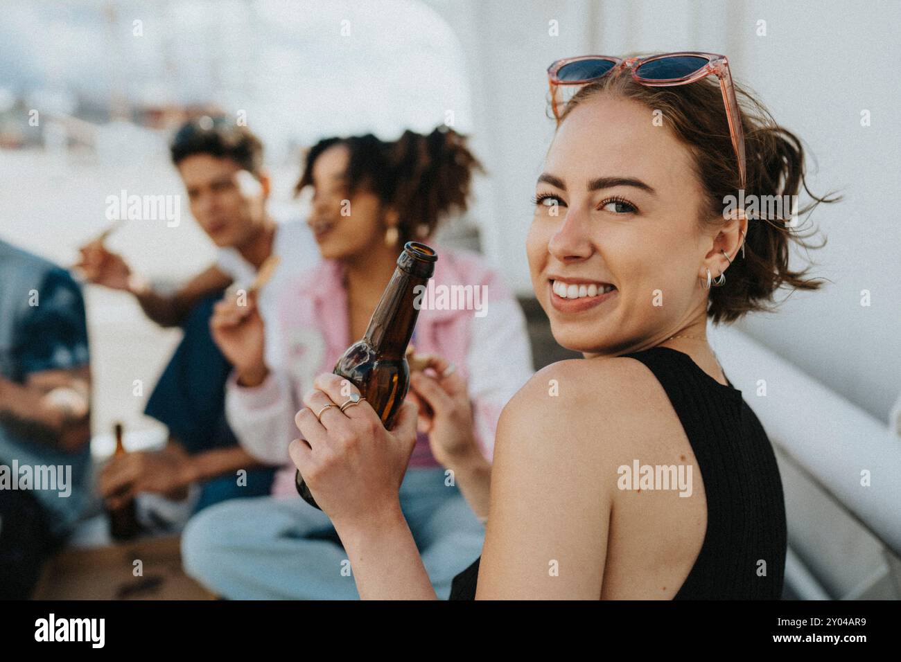 Porträt einer schönen jungen Frau, die eine Bierflasche hält, während sie über die Schulter auf den Parkplatz schaut Stockfoto