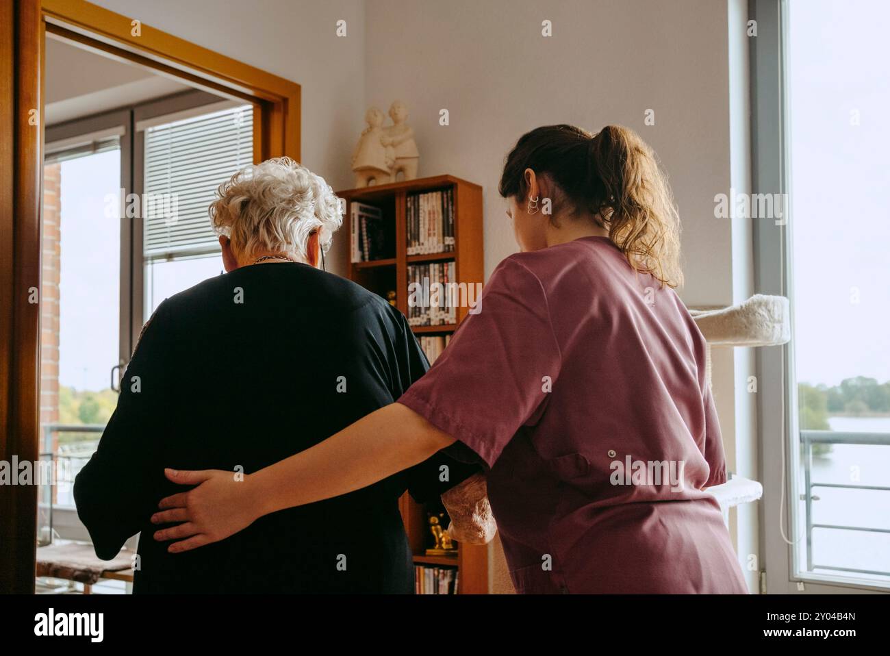 Rückansicht einer Pflegeperson, die eine Seniorin beim Gehen in der Wohnung unterstützt Stockfoto