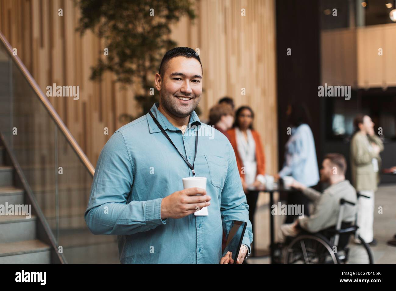 Porträt eines lächelnden männlichen Delegierten, der während der Kaffeepause im Convention Center eine Einwegtasse hält Stockfoto