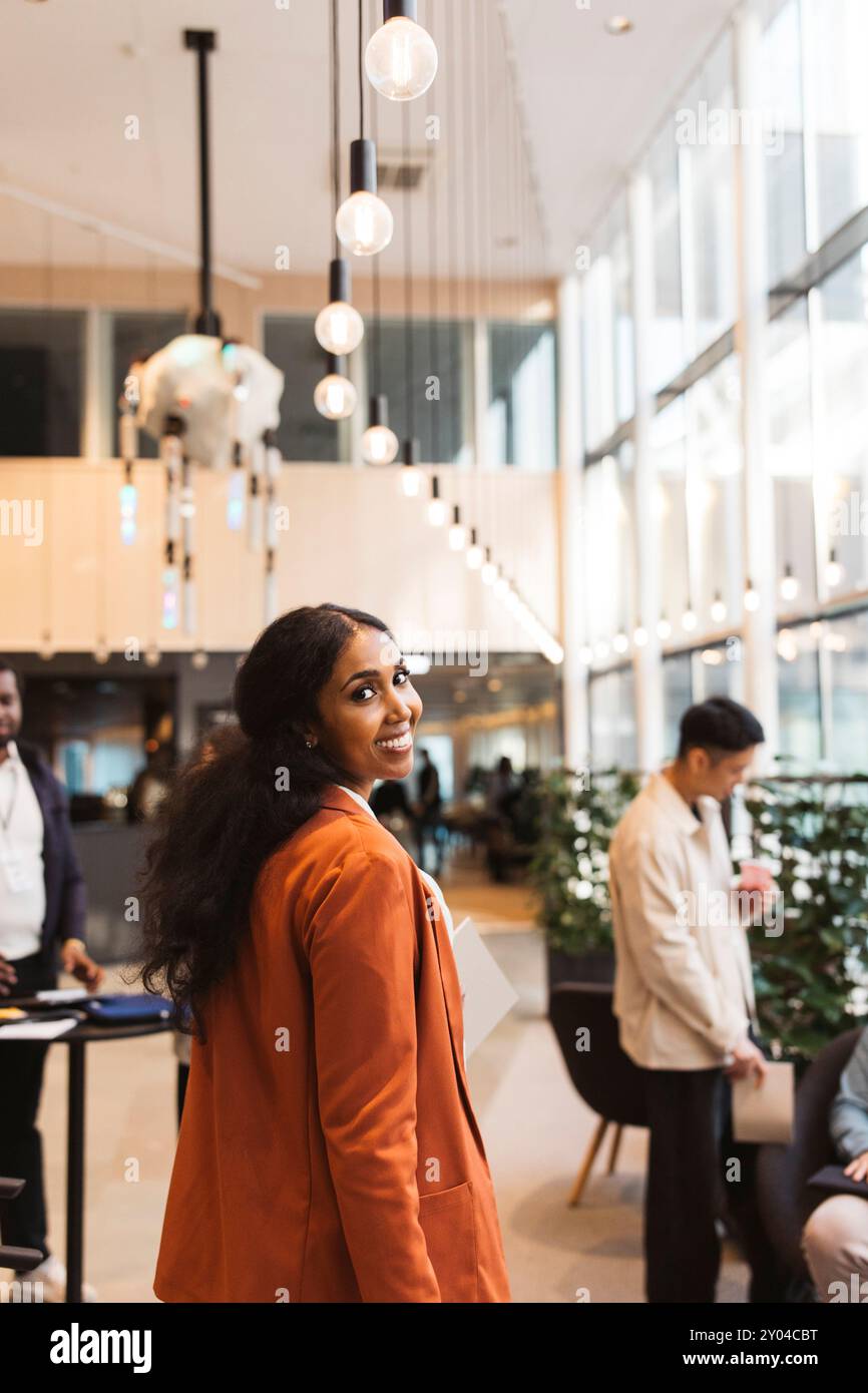 Porträt einer lächelnden Unternehmerin, die über die Schulter schaut, während sie in der Lobby im Convention Center spaziert Stockfoto