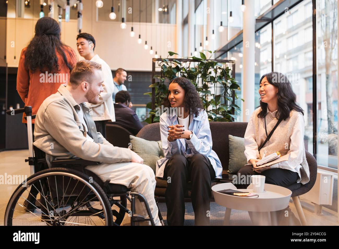 Junge Unternehmerin mit Behinderung hört weiblichen Delegierten zu, die während des Seminars auf der CON Geschäftsstrategie erklären Stockfoto