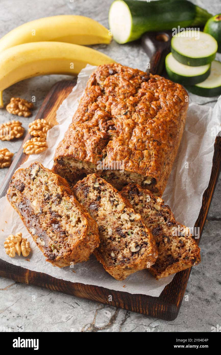 Banana Zucchini Brot mit Walnüssen und dunkler Schokolade auf dem Holzbrett auf dem Tisch. Vertikal Stockfoto