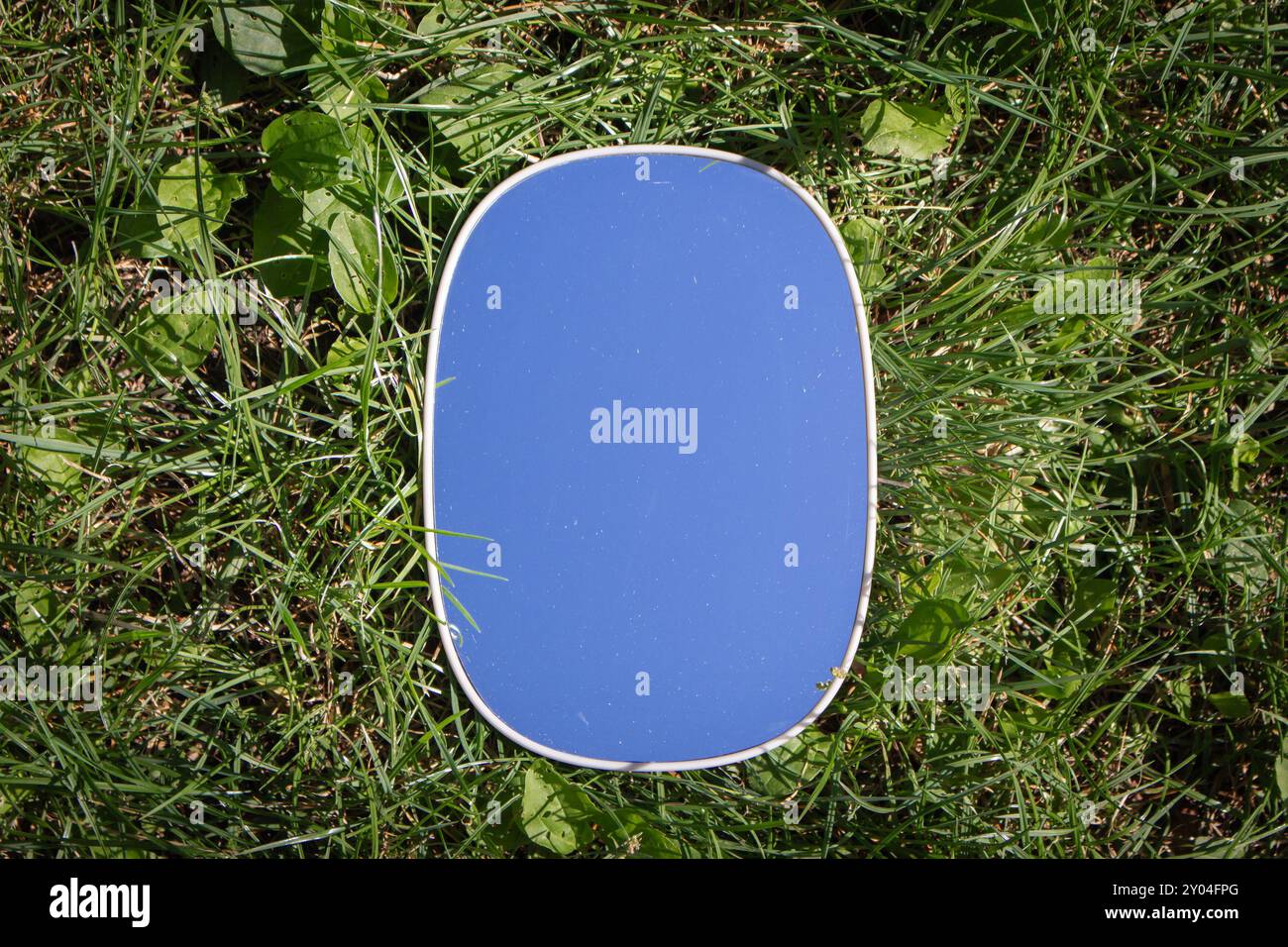 Ovaler Spiegel auf grünem Gras mit Kopierraum. Gras- und Himmelsspiegelung im Spiegel. Ökologisches Konzept. Spiegel auf grünem Rasen. Fragilität der Natur. Stockfoto