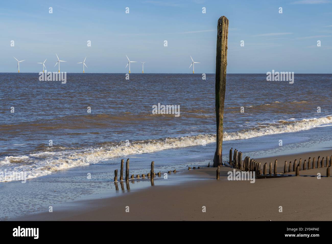 Nordseeküste in Caister-on-Sea, Norfolk, England, Großbritannien, mit den Überresten eines Wellenbrechers am Strand und Windturbinen im Hintergrund Stockfoto