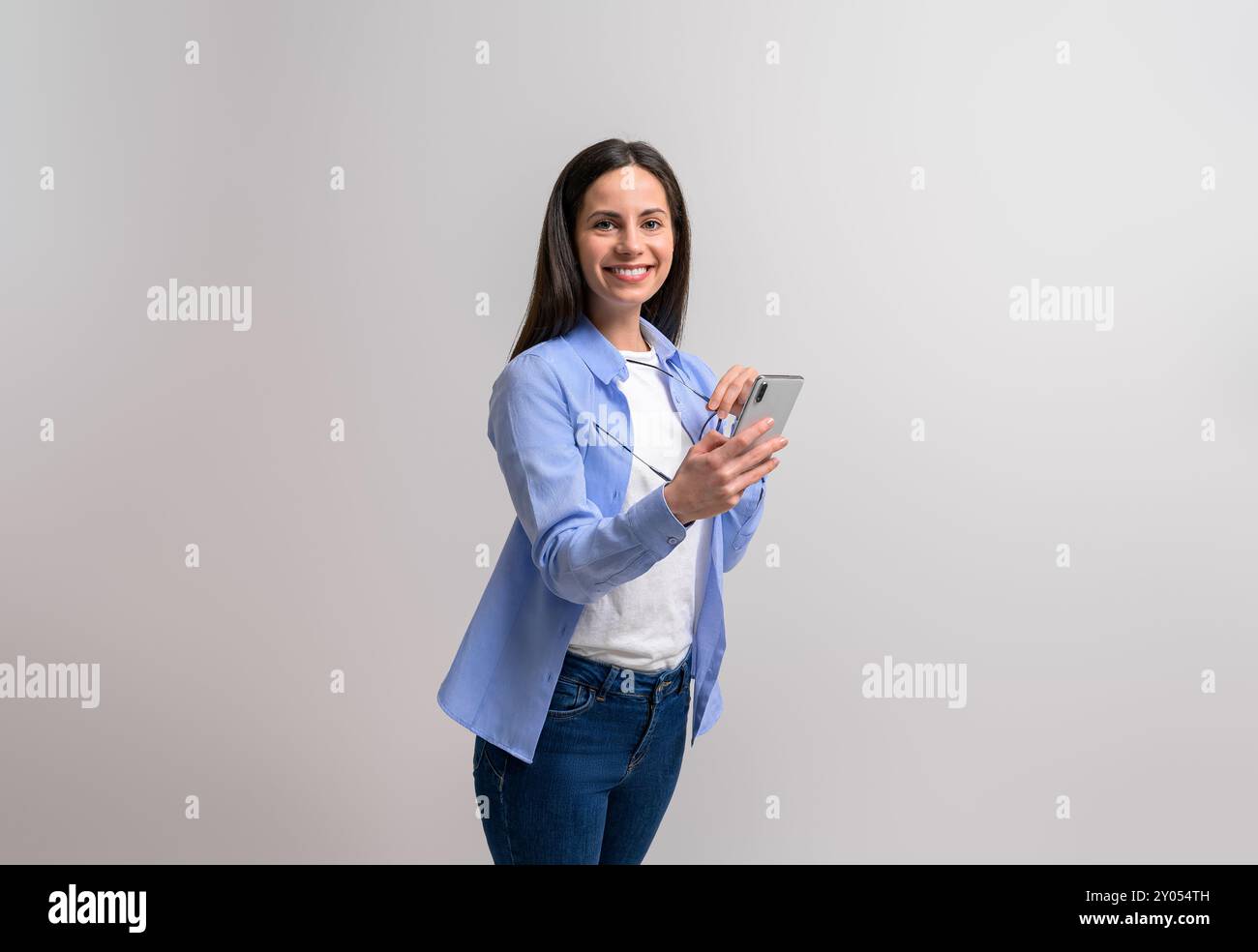 Porträt einer lächelnden jungen Geschäftsfrau, die Handy und Brille vor weißem Hintergrund hält Stockfoto